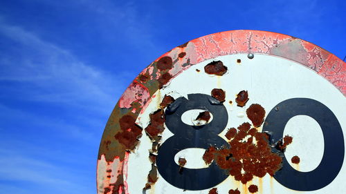 Low angle view of rusty metallic sign structure against blue sky