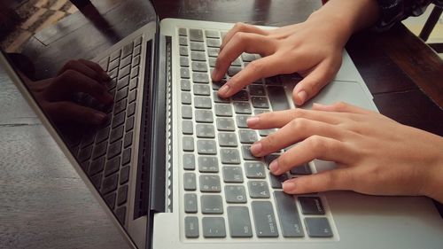 Cropped hands of woman using laptop on desk