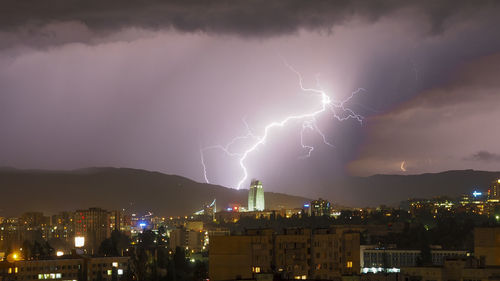 Lightning over illuminated buildings in city at night
