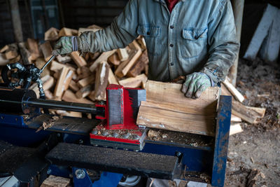 Hydraulic log splitter blade cuts into wood with workman and defocused woodpile