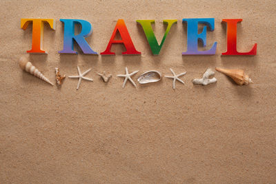 Directly above shot of travel text with seashells on sand at beach