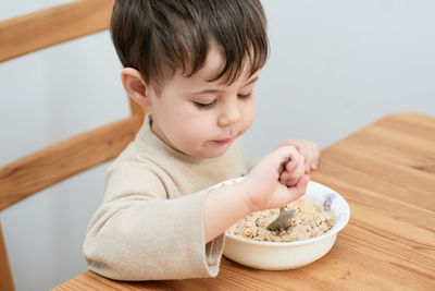 Little boy eating oatmeal for breakfast in the kitchen