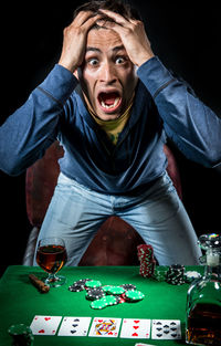 Portrait of shocked man standing at poker table with whiskey against black background