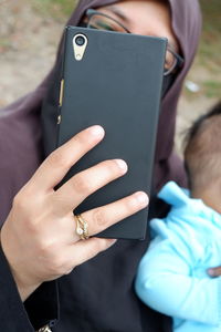 Mother wearing hijab taking selfie with daughter while sitting outdoors
