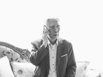 Senior man talking on mobile phone while sitting on sofa against white background