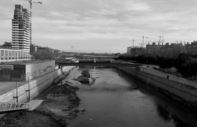 Bridge over river by buildings in city against sky