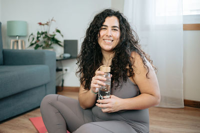 Portrait of young woman holding water bottle at home