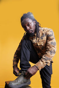 Portrait of young man sitting against yellow background