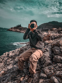 Man photographing on rock by sea against sky