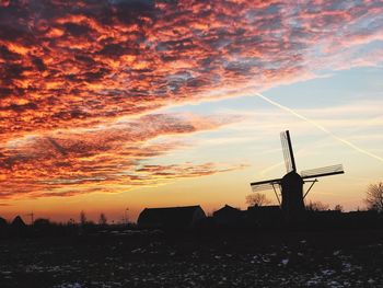 Silhouette traditional windmill on field against sky at sunset