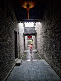 Woman holding umbrella while standing in alley