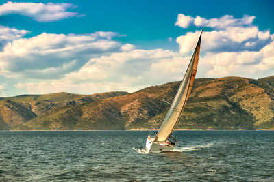 Boat sailing on sea by mountain against sky