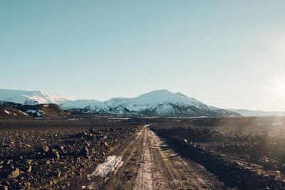 Dirt road amidst field leading towards mountain against sky