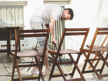 A caucasian guy washes leaning wooden garden chairs with karcher