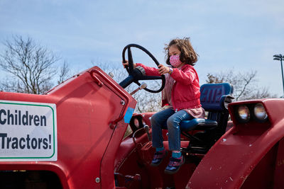 Girl in a mask pretending to drive a tractor at the county fair exhibit