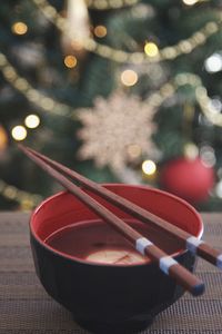 Close-up of bowl with chopsticks against christmas tree on table