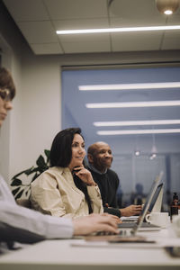 Smiling businesswoman with male and female colleagues discussing while working late at office