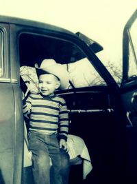 Rear view of boy sitting in car against sky