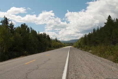 Empty road amidst trees against sky