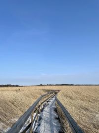 Road amidst field against clear blue sky