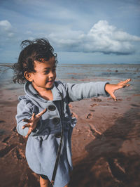 Young woman standing at beach against sky