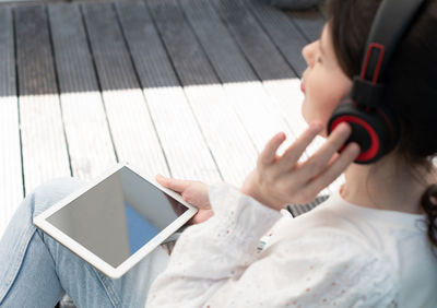 A young girl sadly listens to music in headphones using a tablet