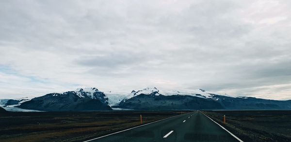 Road leading towards snowcapped mountains against sky