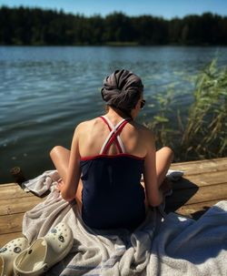 Rear view of woman sitting on rock by lake