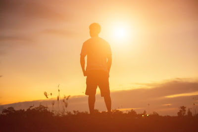 Rear view of silhouette man standing on field against sky during sunset