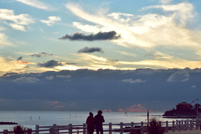 Silhouette people standing by sea against sky during sunset