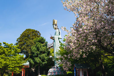 Low angle view of statue amidst flowering plants against sky