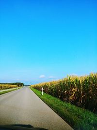 Road amidst field against clear blue sky