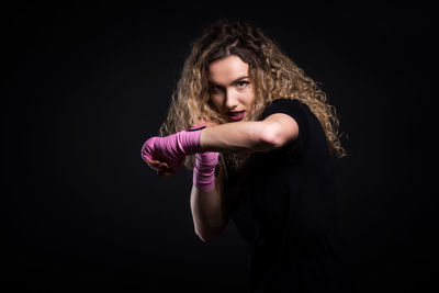 Portrait of female boxer standing against black background