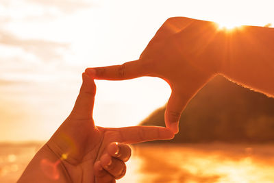 Cropped hands of child making finger frame against sea