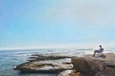 Full length of man sitting on chair by sea against sky