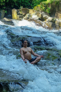 Full length of shirtless young man looking at sea