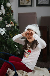 Portrait of girl making heart shape while sitting at home during christmas