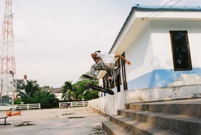 Man jumping while skateboarding against building and sky