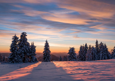 Snow covered landscape against sky during sunset
