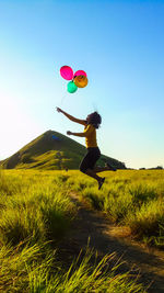 Woman with balloons jumping on land against blue sky