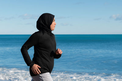 Portrait of young woman standing at beach against sky