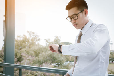 Businessman checking time in wristwatch against sky