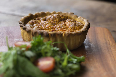 Close-up of savory pie slice with salad on wooden plate