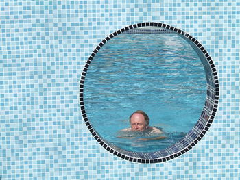 Senior man swimming in pool seen through circle