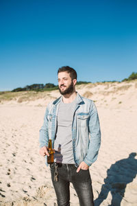 Full length of young man standing at beach against clear sky