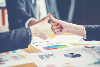 Business people gesturing thumbs up over graphs and desk at office