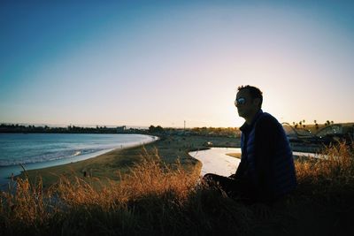 Side view of man sitting on grass by beach