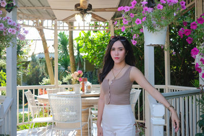 Portrait of young woman standing by potted plants