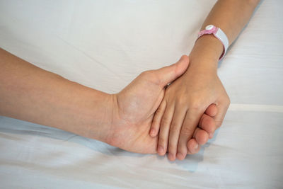 High angle view of people holding hands on bed at hospital