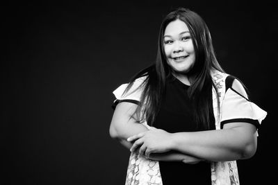 Portrait of smiling young woman against black background